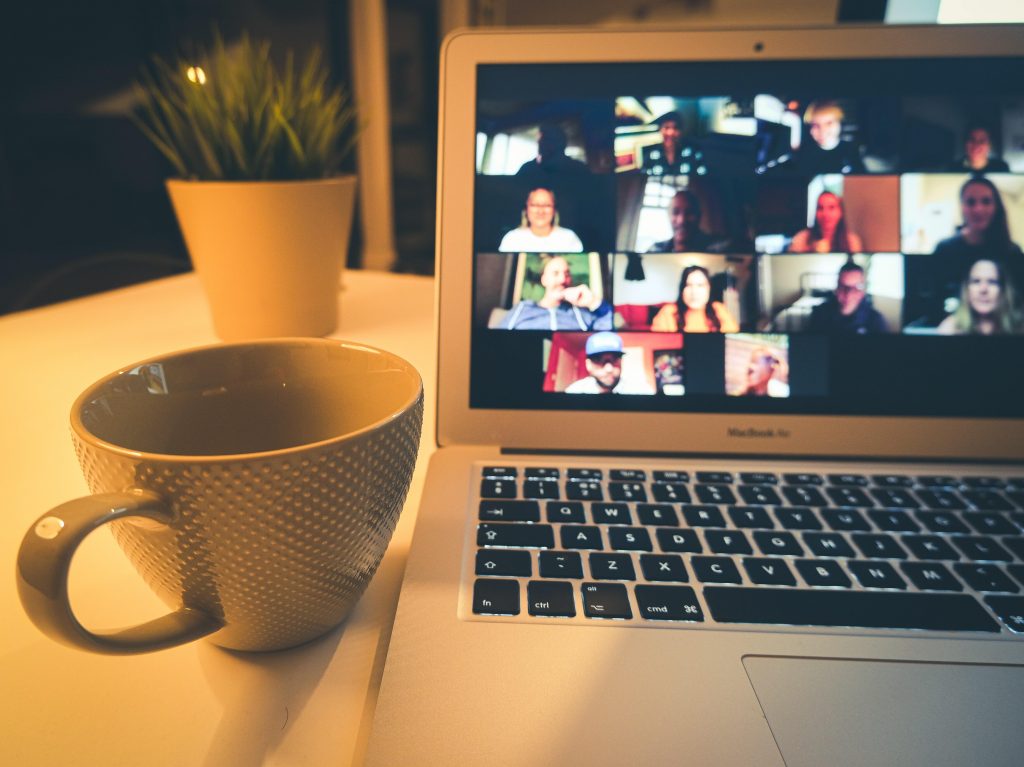 An open laptop picturing an online meeting, with a mug and plant next to it. 